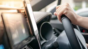 Pessoa segurando volante do carro com celular preso ao painel